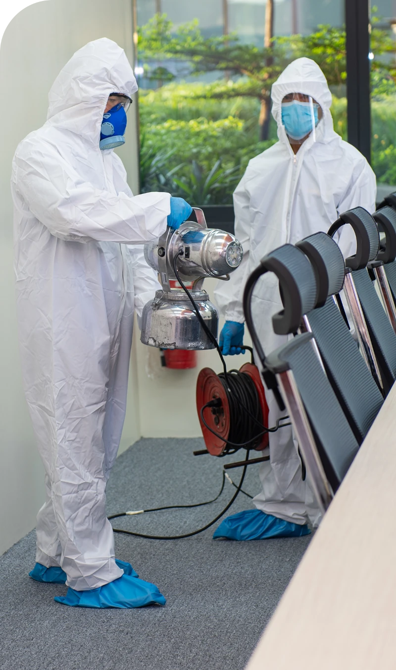 Two workers in protective gear and masks are focused on a machine, highlighting safety protocols in their task.